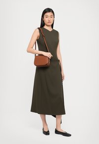 Olivově zelené šaty bez rukávů se rovný střihem, délka do poloviny lýtek, kombinované s hnědou crossbody kabelkou a černými plochými botami.
