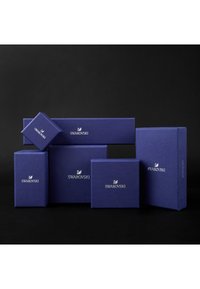 Set aus blauen strukturierten Geschenkboxen mit silbernem "Swarovski"-Logo in unterschiedlichen Größen, mit rechteckiger Form und klaren Linien, vor einem dunklen Hintergrund präsentiert.