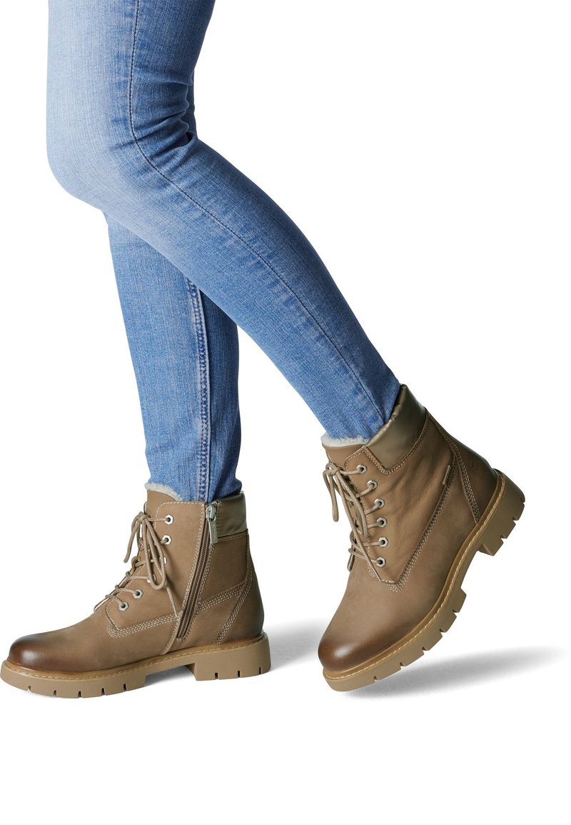 Bottines en cuir marron avec un design à lacets, finition texturée et col rembourré. Comprend une fermeture éclair latérale et une semelle robuste. Associées à un jean bleu.