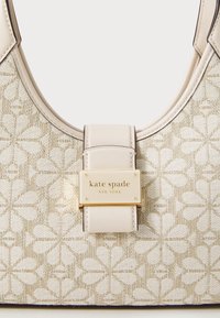Beige fabric handbag with floral pattern, smooth leather accents, a gold plaque featuring "Kate Spade New York," and a curved top handle.