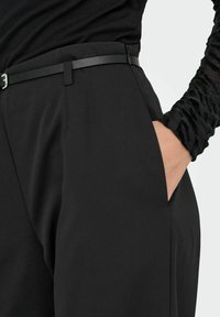 Czarne dopasowane spodnie o gładkiej, gładkiej teksturze, z wąskim czarnym paskiem i bocznymi kieszeniami. Widać regulowany pas.