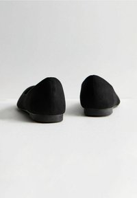 Bailarinas de ante negro con puntera redondeada y tacón bajo, que presentan un exterior suave y costuras sutiles. Diseño minimalista con una silueta clásica.