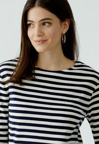 Marineblauwe en crèmekleurige gestreepte langemouwen shirt met een ronde hals. Heeft een zachte stof en subtiele stikseldetails.