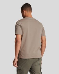 T-shirt kratkih rukava, s okruglim izrezom, u bež pamuku, s glatkom teksturom i opuštenim krojem, nosi se s zelenim cargo hlačama.