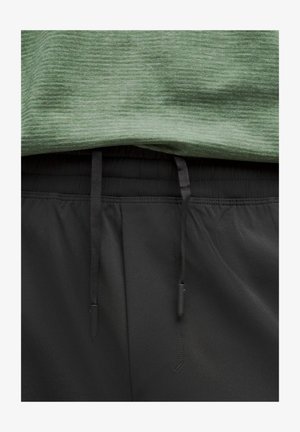 Vihreä urheilupaita, jossa on teksturoitu pinta, kerrostettuna mustien shortsien päälle, joissa on naru- ja sileä kangas.