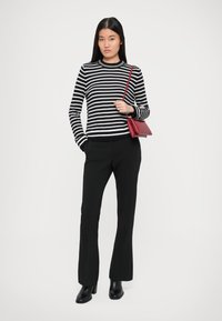 Black and white striped sweater with ribbed neckline, paired with black flared trousers and black ankle boots; red crossbody bag.
