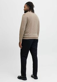 Tannfärgad stickad tröja med lång ärm, parat med svarta byxor. Outfiten har en avslappnad passform och subtil textur, ihop med svarta skor.