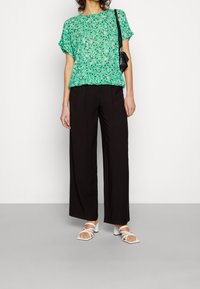 Top corto de flores verdes de manga corta combinado con pantalones negros de pierna ancha y sandalias blancas de tacón bloque. Presenta un ajuste holgado y un diseño relajado.