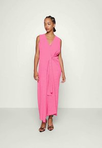 Vestido rosa sem mangas com decote em V e detalhe torcido na cintura. Design longo e fluido com uma textura suave e fenda lateral.