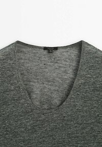 Szary sweter z dekoltem w serek o fakturowanym wzorze dzianiny. Luźny fason, z prostym, czystym wykończeniem dekoltu oraz subtelnymi ciemnymi plamkami rozmieszczonymi na całej powierzchni.