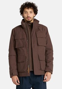 Giacca isolata marrone con chiusura a zip, bottoni a pressione, più tasche frontali e un colletto alto per un maggiore calore.