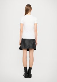 Valge lühikeste varrukatega T-särk, millele on sobitatud must nahast mini-seelik, millel on lukud ja küljetasku. Lihtne disain, sile tekstuur.