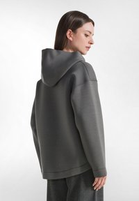 Felpa grigia con cappuccio, dalla vestibilità rilassata, texture morbida e polsini a costine. Presenta un cappuccio con cordini e un design minimalista.