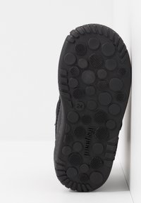 Suola di scarpa nera in gomma con una presa testurizzata, caratterizzata da vari motivi circolari e testurizzati. Design robusto con una leggera curvatura verso l'alto.