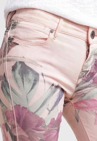 Spijkerbroek van lichtroze denim met bloemenpatroon. Voorzien van voorzakken, metalen knopen en een gladde textuur met levendige tinten.