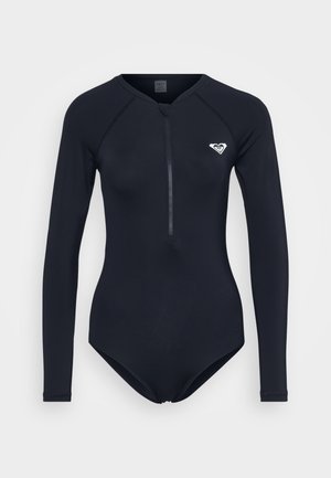 Garais piedurkņu tums zilā neoprēns uzvalks ar priekšējo rāvējslēdzēju un mazu baltu logo kreisajā krūtī. Izgatavots no elastīga, gluda materiāla.