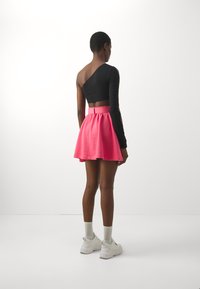 Svart en-skulder crop-top som er parret med et rosa skater skjørt med en sløyfe i midjen. Hvite joggesko og lysegrå sokker fullfører antrekket.