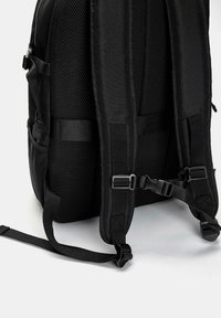 Gros plan sur le panneau arrière d'un sac à dos noir et les bretelles rembourrées avec des fermetures à boucles réglables et un rembourrage en mesh pour le confort.
