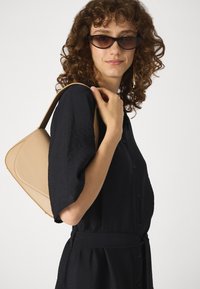 Black button-up dress with short, puffed sleeves. Features a beige, curved handbag resting on the shoulder. Black, angular sunglasses.