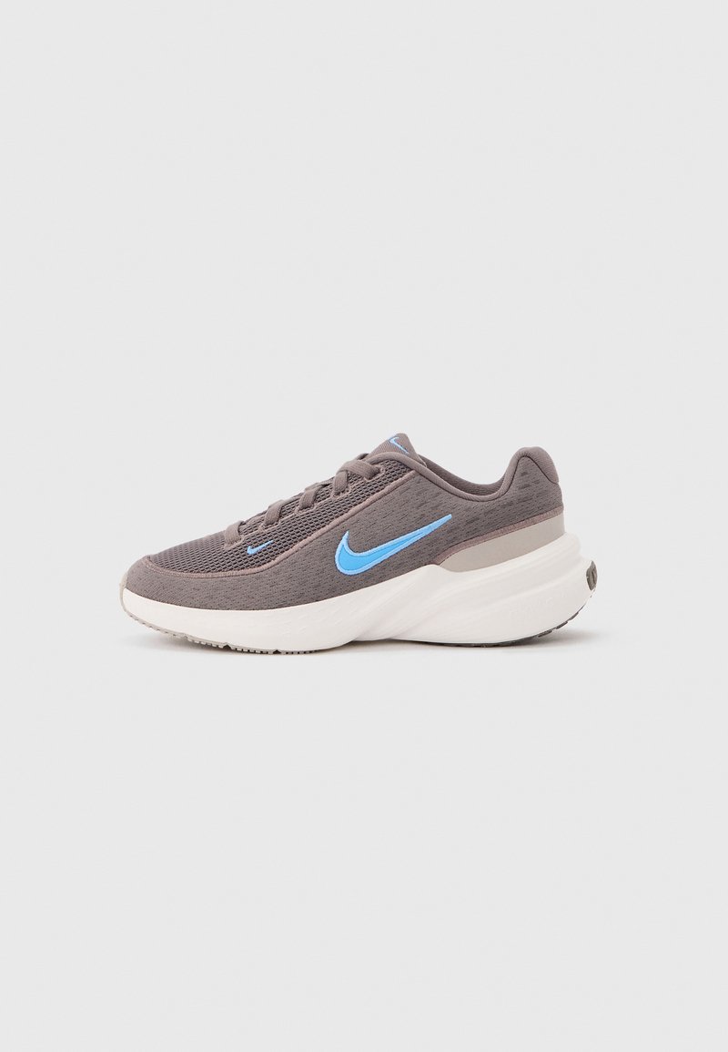 Γκρι παπούτσι Nike για τρέξιμο με ανοιχτό μπλε λογότυπο Swoosh, πλέγμα επάνω μέρος και παχύ λευκό πάτο, εμφανίζεται από το πλάι σε γκρι φόντο.