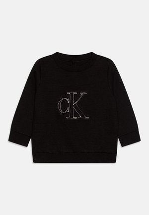 Pull en maille noir à manches longues avec col rond, poignets et ourlet côtelés, arborant un grand logo "cK" blanc en contour au centre avant.
