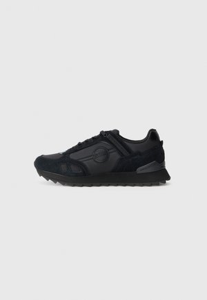 Schwarze Sneaker aus einer Kombination von glattem Leder und strukturiertem Wildleder, mit einem runden Logo, Gummisohle und dreieckigem Profil.