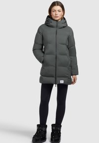 Cappotto imbottito grigio scuro, lungo fino al ginocchio, con colletto alto e cappuccio, dotato di cerniera frontale e tasche laterali, indossato su leggins neri e stivali.