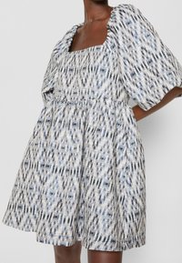 Puffärmsklänning i ett mönstrat tyg med blå, vita och svarta nyanser, med fyrkantig halsringning och volang i midjan.