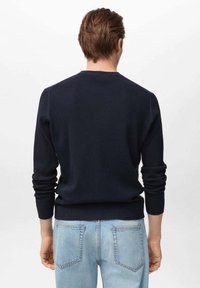 Suéter de punto de marina con mangas largas, cuello redondo y puños ajustados. Combinado con jeans de mezclilla azul claro con bolsillos traseros.