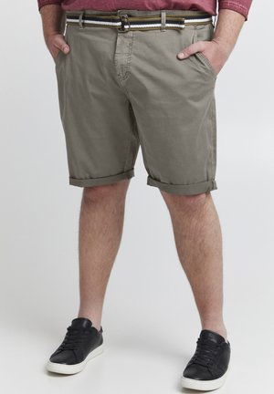 Shorts kaki avec un ourlet replié, dotés de poches latérales et d'une ceinture tressée avec des accents marron, noir et blanc. Portés avec des baskets noires.