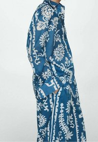 Ensemble chemise et pantalon bleu à motifs, fabriqué en tissu léger. Présente des motifs floraux et géométriques blancs, avec des boutons et des poches.