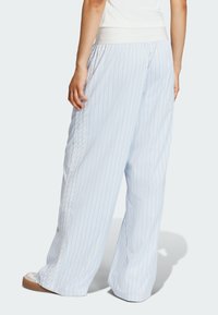 Jasnoniebieskie spodnie w paski o luźnym kroju, z elastycznym pasem i bocznymi detalami. Spodnie mają gładką teksturę i szerokie nogawki.