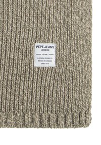 Tejido de punto acanalado beige con una superficie texturizada, que presenta una etiqueta blanca con "PEPE JEANS LONDON" e información sobre la marca.