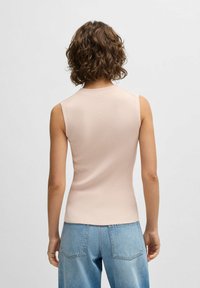 Vaaleanpunainen ribattu hihaton toppi, jossa on korkea kaula-aukko ja tiukka muotoilu, yhdistettynä vaaleansinisiin farkkuihin. Takakatsaus, jossa on yksinkertainen tyyli.