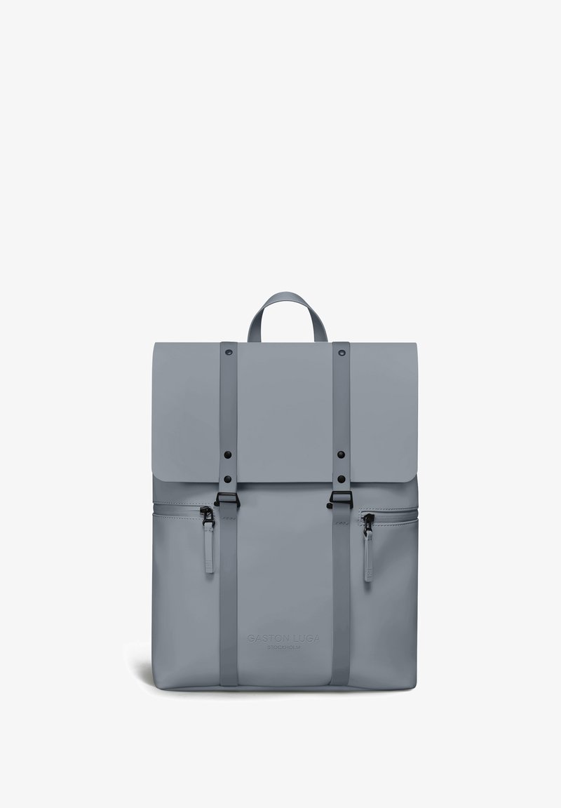 Sac à dos rectangulaire gris clair avec fermeture à rabat, deux sangles verticales avec boucles, deux poches latérales zippées et poignée supérieure.
