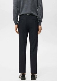 Pantaloni blu navy scuro con una vestibilità su misura, caratterizzati da una texture liscia, tasche posteriori e una piega lungo la parte frontale. Abbinati a scarpe nere.