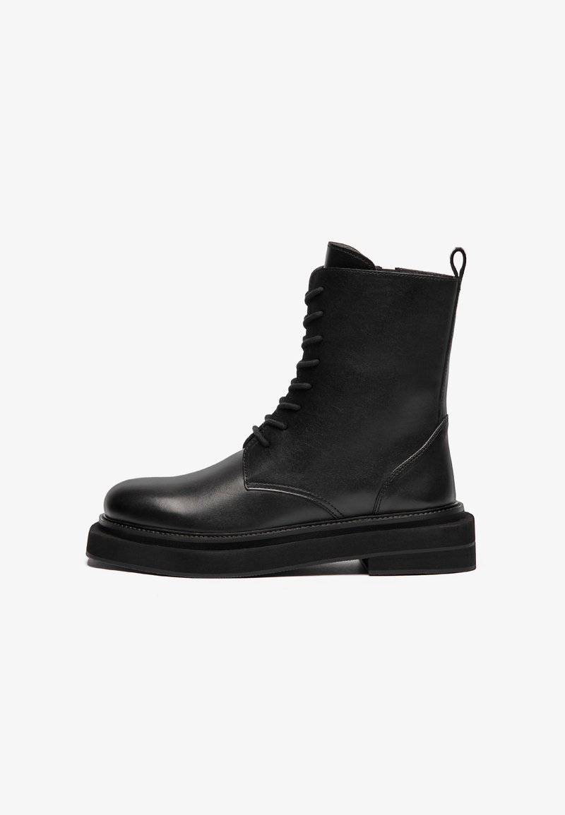 Bottine noire en cuir à lacets avec semelle épaisse et languette arrière, vue de profil sur fond blanc.