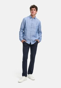 Lys blå lin skjorte med knapper, lange ermer og en liten logo. Kombinert med marineblå bukser og hvite joggesko.