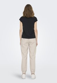 Haut noir à manches courtes avec un col rond, associé à un jogging beige à taille élastique, doté de poignets aux chevilles et de baskets blanches.