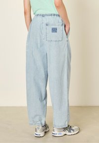 Ljusblå denim baggybyxor med elastiskt midjeband, featuring sidofickor och en bakficka med en blå "American Vintage"-etikett.