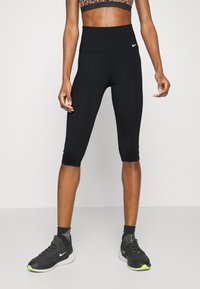 Leggings negras recortadas con una cinturilla alta, hechas de material elástico, combinadas con zapatillas deportivas negras con acentos neón.