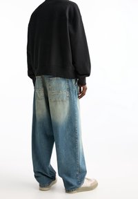 Felpa nera oversize con spalle scese, abbinata a jeans in denim chiaro, a gamba larga e scoloriti, e sneakers color crema. Design semplice.