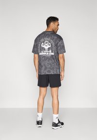 Γκρι t-shirt με τεχνική βαφής tie-dye και λευκό γραφικό, που απεικονίζει ένα καρτούν και κείμενο, συνδυασμένο με μαύρο σορτς και μαύρα αθλητικά παπούτσια.