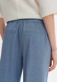 Pantalon texturé bleu clair avec une taille élastique, comprenant deux poches arrière et une coupe décontractée. Le matériau semble tissé.