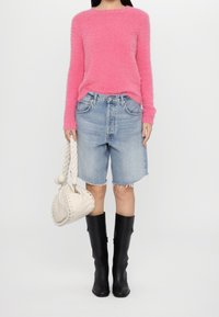 Puszysty różowy sweter, dżinsowe szorty bermudy z postrzępionymi brzegami, czarne kozaki do kolan oraz pleciona kremowa torebka o zaokrąglonym kształcie.