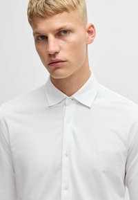 Chemise blanche à manches longues en tissu lisse, dotée d'un col classique, d'une fermeture à boutons et de détails discrets de logo ton sur ton.