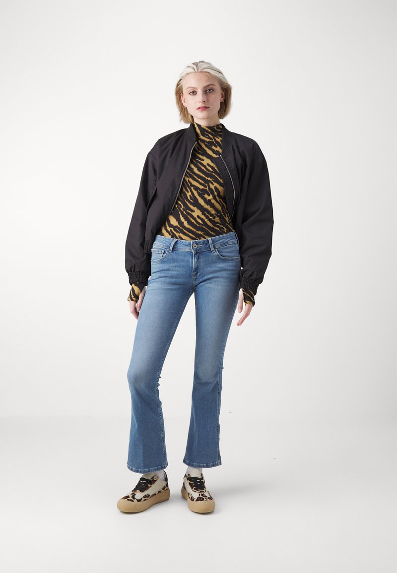 Veste bomber noire sur un col roulé imprimé à motifs rayés de tigre, associée à un jean évasé bleu clair et des chaussures à motifs.