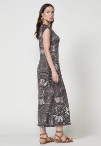 Maxikleid aus dunkelbrownem Stoff mit einem komplexen weißen und rosa Muster. Kurzärmel und ein tailliertes Oberteil führen zu einem fließenden Rock.