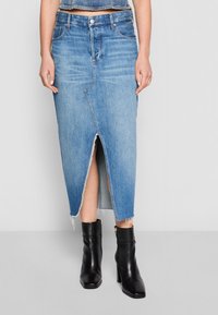 Falda midi de mezclilla en azul claro con una abertura central, dobladillo deshilachado y forma estructurada. Combinada con botines negros de tacón.