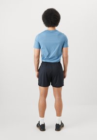 Blå kortermet treningsskjorte og svarte shorts. Skjorten har en glatt tekstur. Shortsene har elastisk midje og sidelommer.